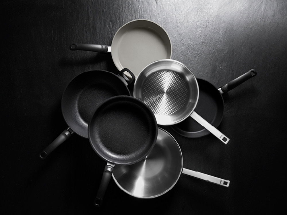 Eine gestapelte Anordnung verschiedener Bratpfannen, die unterschiedliche Materialien und Texturen präsentieren.