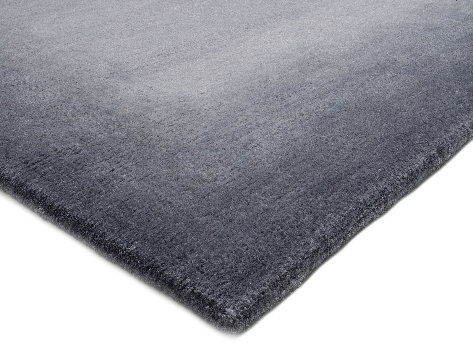 Grauer Wollteppich in Nahaufnahme, perspektivisch von der Seite fotografiert.