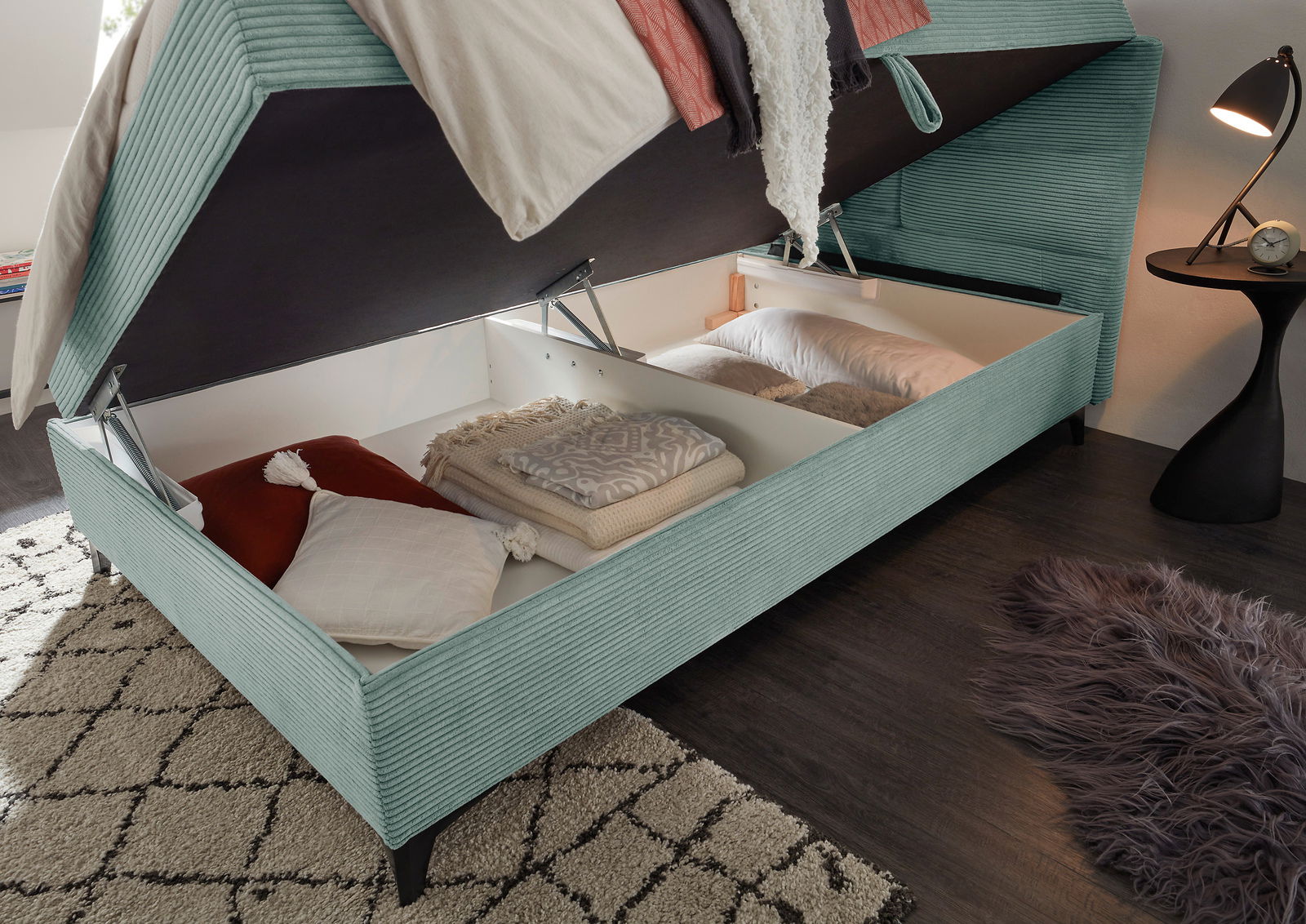 Boxbett mit geöffnetem Stauraum, gefüllt mit Kissen und Decken, aus seitlicher Perspektive fotografiert.