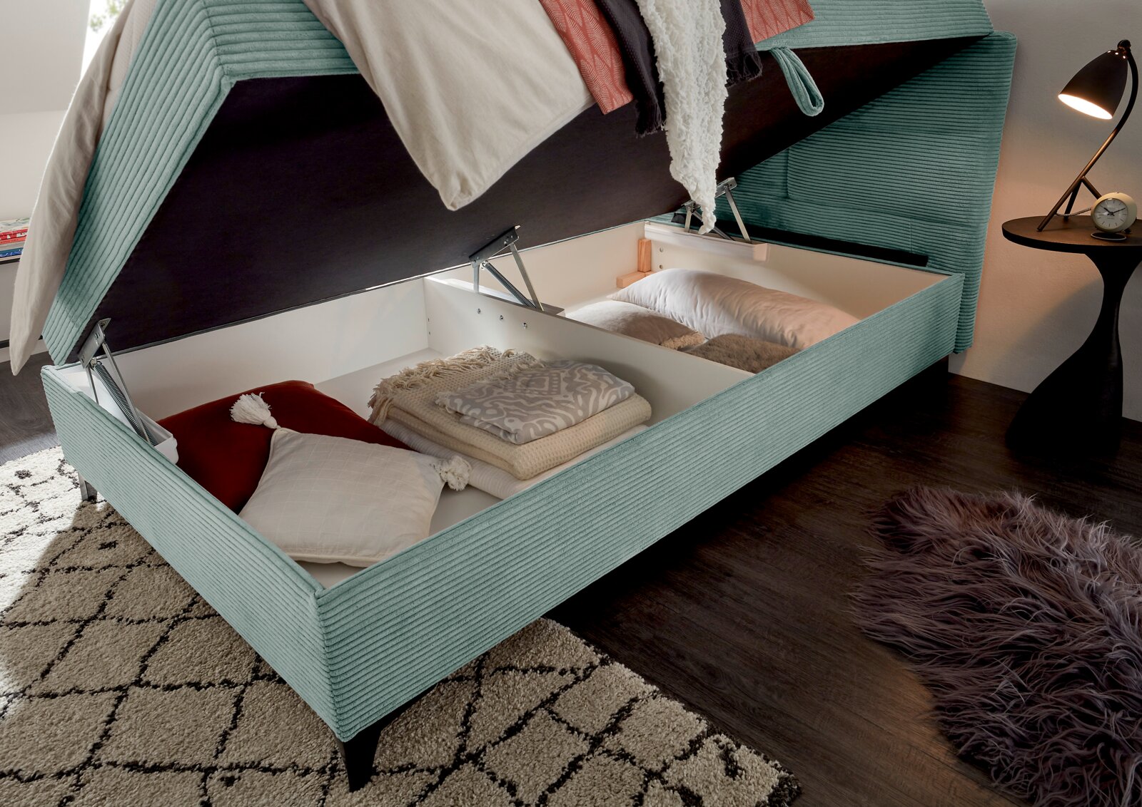 Boxbed met open opbergruimte, gevuld met kussens en dekens, gefotografeerd vanuit een zijaanzicht.