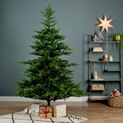 Künstlicher Weihnachtsbaum mit einer Höhe von 150 cm und einem Durchmesser von 111 cm, dekoriert mit Geschenken darunter, in einem modernen Wohnzimmer mit Regal und Dekorationen, seitliche Perspektive.