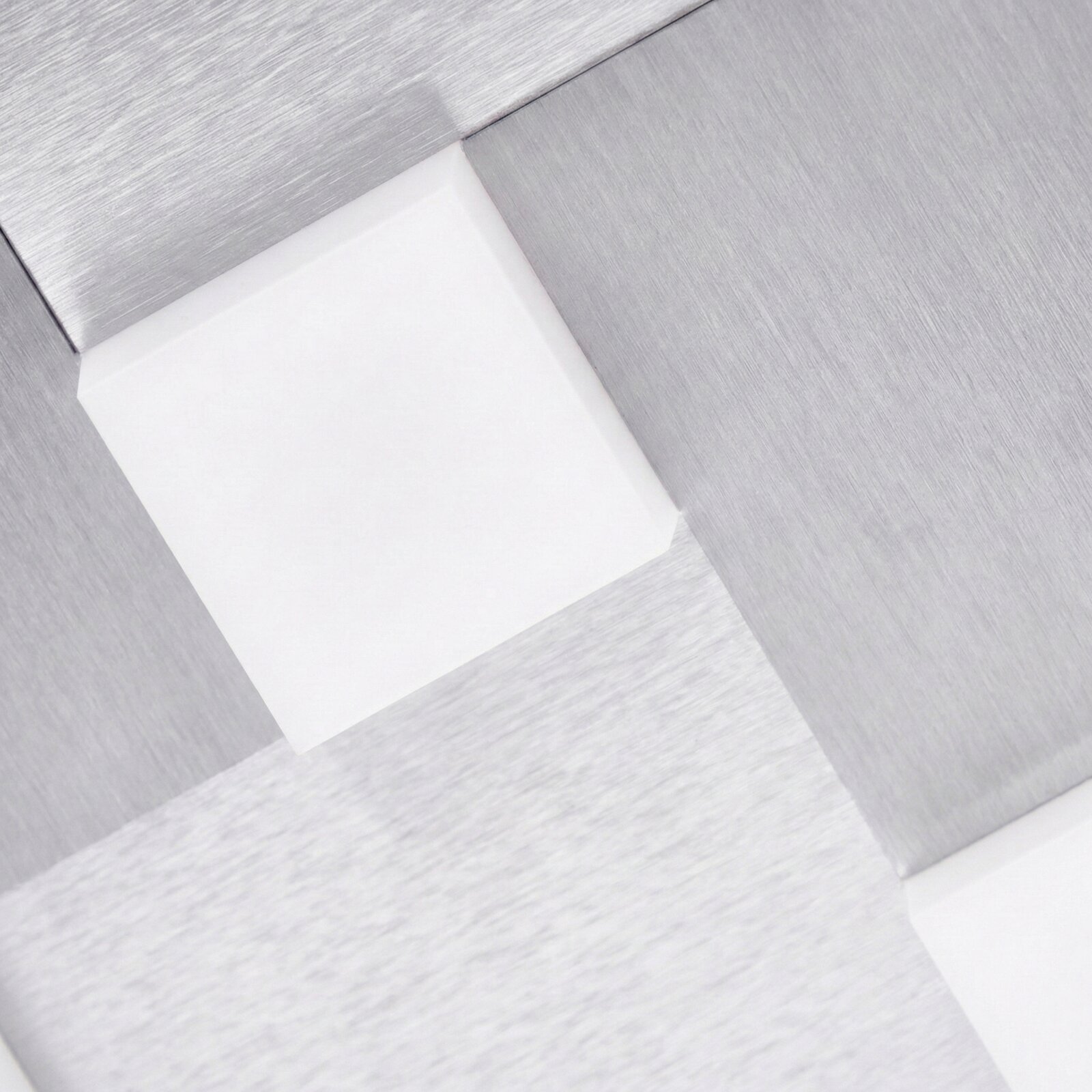 Detailansicht aus schräger Perspektive auf eine moderne geometrische Leuchte mit gebürsteten silberfarbenen Metallflächen und weiß leuchtenden Aussparungen