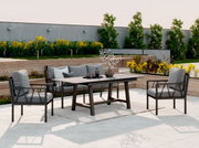 Moderne loungeset en eetset voor buiten met een zwart metalen frame, grijze kussens en een rechthoekige tafel op een lichtgekleurd terras in de tuin; perspectief: licht verhoogd vooraanzicht