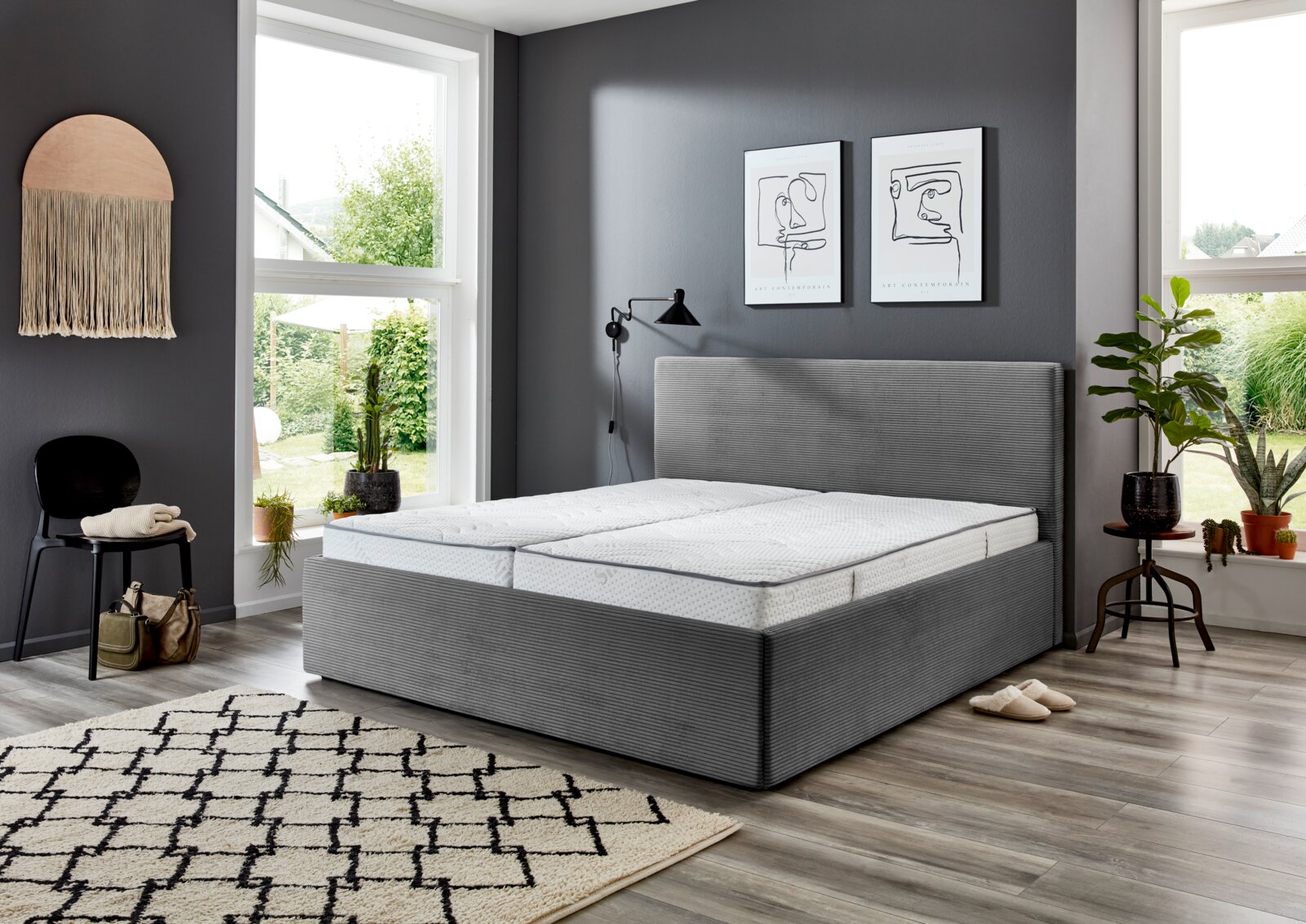 Graues Polsterbett 160x200 in einem modernen Schlafzimmer mit großen Fenstern, Pflanzen und Wanddekorationen, seitliche Perspektive.