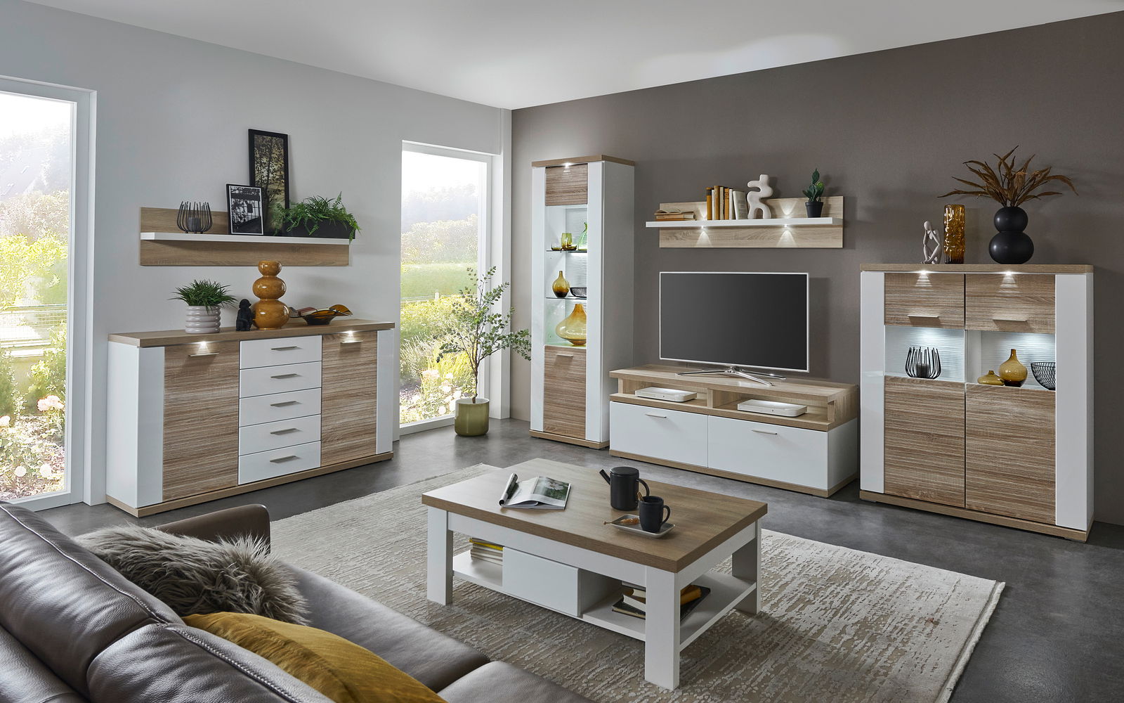 Moderne Wohnzimmer-Wandkombination in Holzoptik mit weißen Akzenten, bestehend aus TV-Schrank, Vitrine und Regalen, aus der Perspektive eines gemütlichen Wohnzimmers.