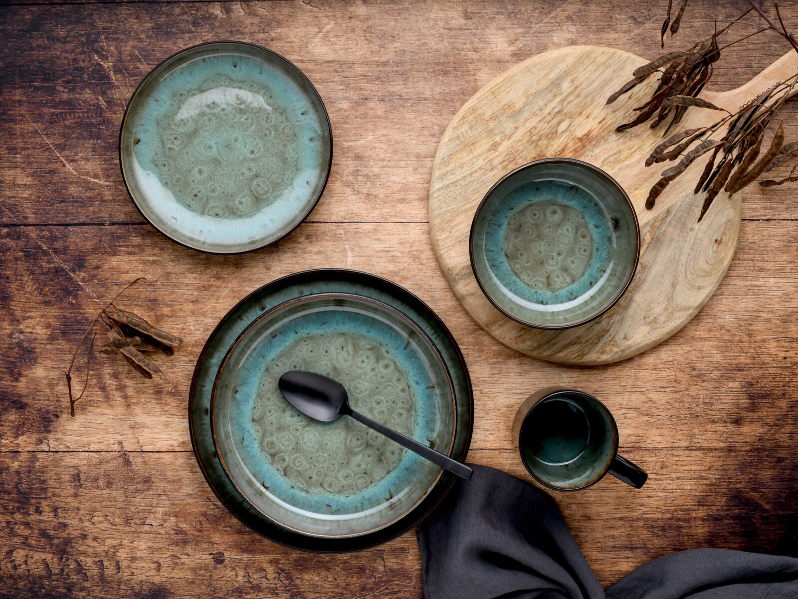 Keramik-Geschirrset in Blaugrün mit Tellern, Schale und Tasse auf rustikalem Holztisch, Draufsicht von oben