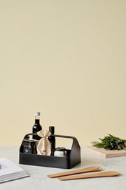 Schwarze Aufbewahrungsbox mit Griff, gefüllt mit verschiedenen Küchenartikeln, auf einem Tisch von schräg vorne fotografiert.