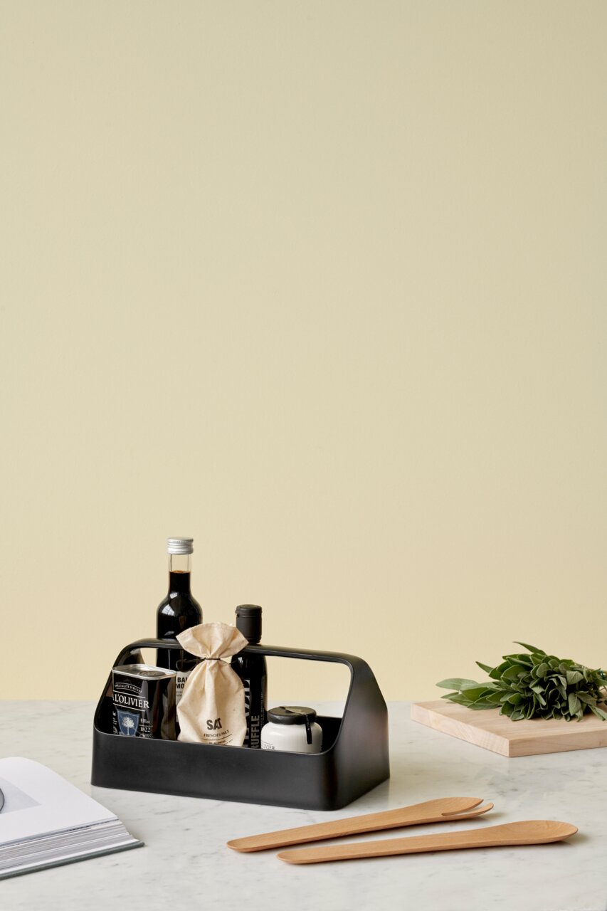 Schwarze Aufbewahrungsbox mit Griff, gefüllt mit verschiedenen Küchenartikeln, auf einem Tisch von schräg vorne fotografiert.