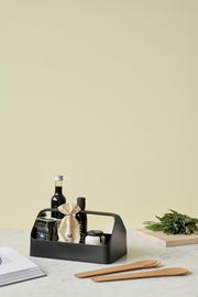 Schwarze Aufbewahrungsbox mit Griff, gefüllt mit verschiedenen Küchenartikeln, auf einem Tisch von schräg vorne fotografiert.