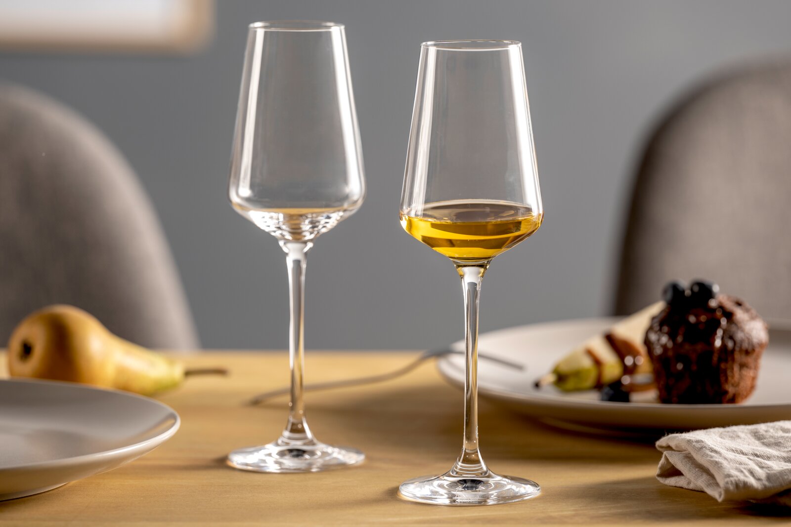 Twee elegante digestiefglazen op een gedekte tafel, waarvan één gevuld met een goudkleurige drank, gezien vanuit de zijkant.