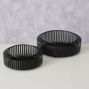 Zwei schwarze, runde Schalen mit vertikalen Streben, auf einer hellen Oberfläche stehend, aus einer leicht erhöhten Perspektive fotografiert.