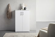 Moderner weißer Schuhschrank mit zwei Türen, frontal fotografiert, dekoriert mit Vasen und einem Buch, neben einer beigen Jacke an der Wand.