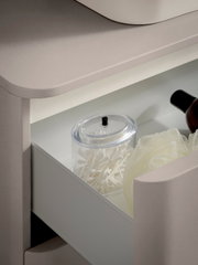 Geöffnete Schublade eines hellen Badezimmermöbels/Waschtischunterschranks mit integriertem LED-Innenlicht, darin ein transparenter Behälter mit Wattestäbchen und ein Badepouf; Perspektive: Nahaufnahme in schräger Seitenansicht von oben.