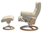Zijaanzicht van een beige fauteuil met bijpassende voetenbank, beide met een frame van hout en metaal.