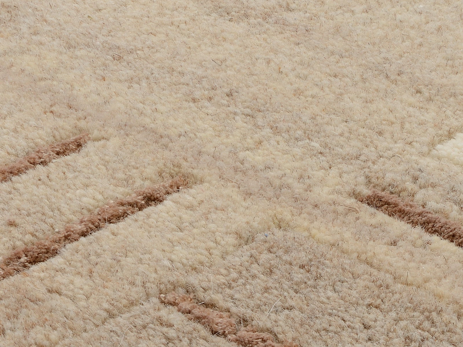 Nahaufnahme eines Wollteppichs mit beigem und braunem Muster, von oben betrachtet.
