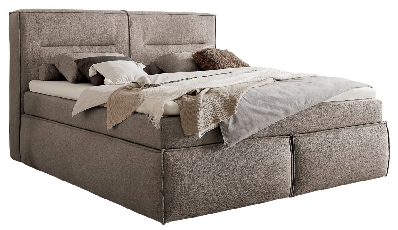 Boxspringbett in seitlicher Perspektive mit grauem Stoffbezug, dekoriert mit Kissen und Decken.