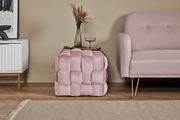 Rosa gepolsterter Hocker in Würfelform, seitlich neben einem Sofa platziert, mit einer Vase und einem Glas darauf.