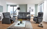 Modernes Wohnzimmer mit einem grauen 3er-Sofa in der Mitte, flankiert von einem Sessel und einem Relaxsessel, mit Blick auf das Meer durch große Fenster.