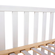 Close-up van een wit babybedje met houten lattenbodem, gezien vanaf de zijkant