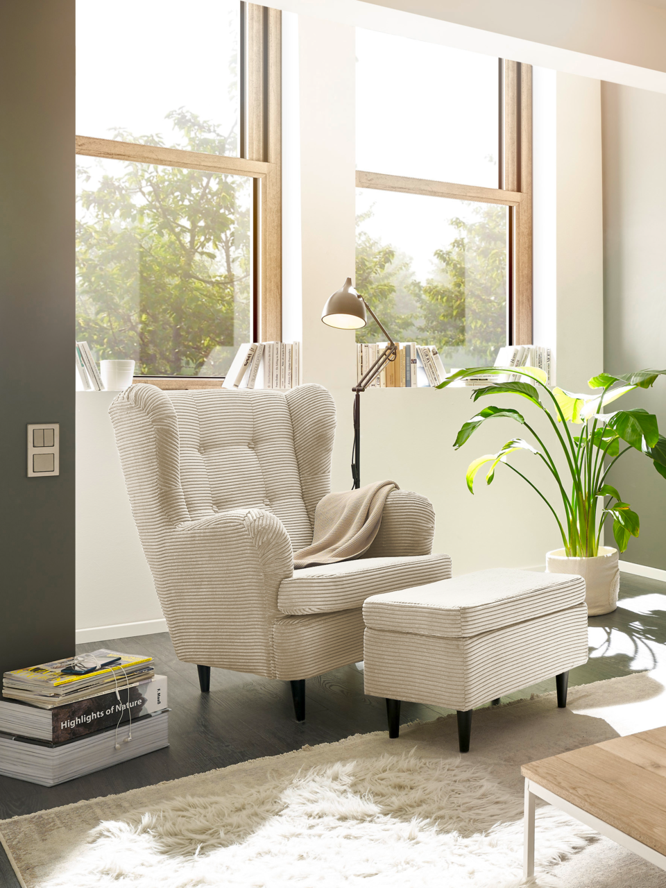 Z2 Hocker OSKAR Hocker in einem modernen Wohnzimmer, seitliche Perspektive, neben einem Sessel und einer Stehlampe, mit großen Fenstern im Hintergrund.