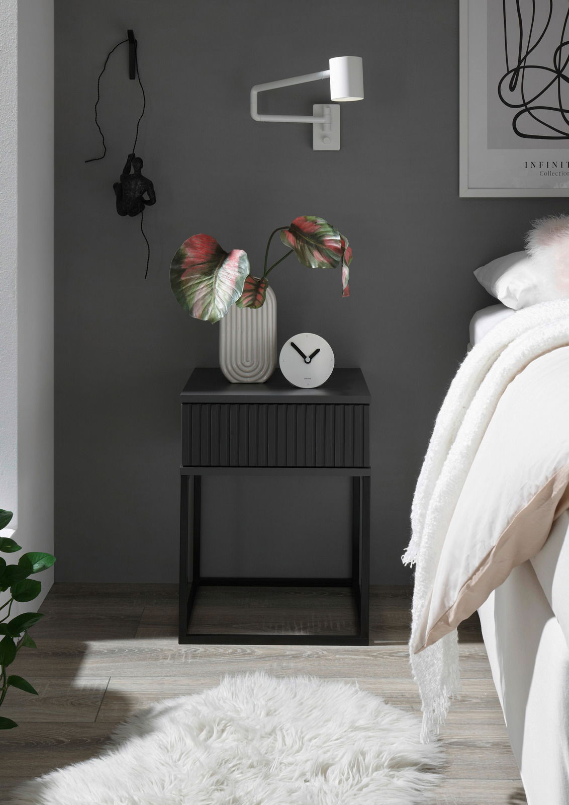 Moderne schwarze Nachtkommode mit geriffelter Front, dekoriert mit einer Vase und einer Uhr, seitliche Perspektive.