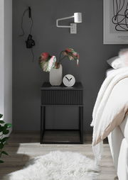 Moderne schwarze Nachtkommode mit geriffelter Front, dekoriert mit einer Vase und einer Uhr, seitliche Perspektive.