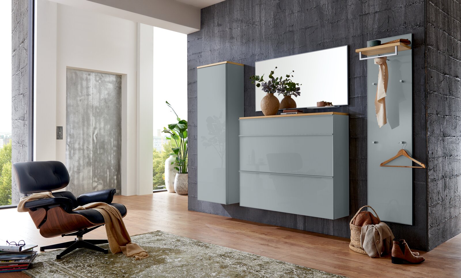 Modernes Flur-Set mit wandhängender Kommode und Hochschrank in grauer Hochglanzoptik mit Holzablage, großem Spiegel und Garderobenpaneel mit Haken und Ablage, frontal aus leicht seitlicher Perspektive im Wohnraum inszeniert