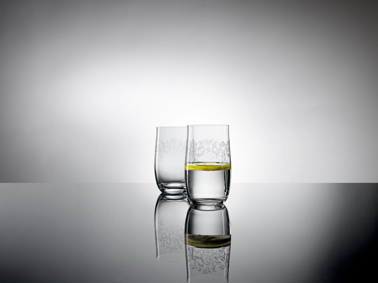 Zwei elegante 380ml Becher mit romantischem Muster, gefüllt mit Wasser und einer Zitronenscheibe, auf einer reflektierenden Oberfläche aus seitlicher Perspektive.