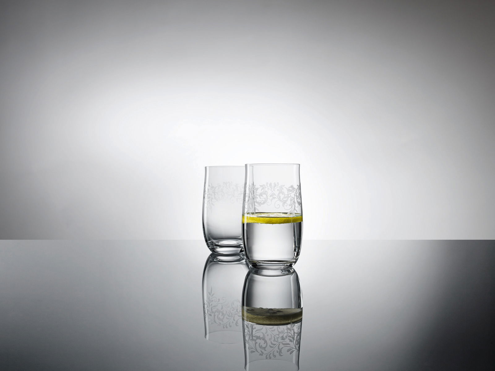 Zwei elegante 380ml Becher mit romantischem Muster, gefüllt mit Wasser und einer Zitronenscheibe, auf einer reflektierenden Oberfläche aus seitlicher Perspektive.