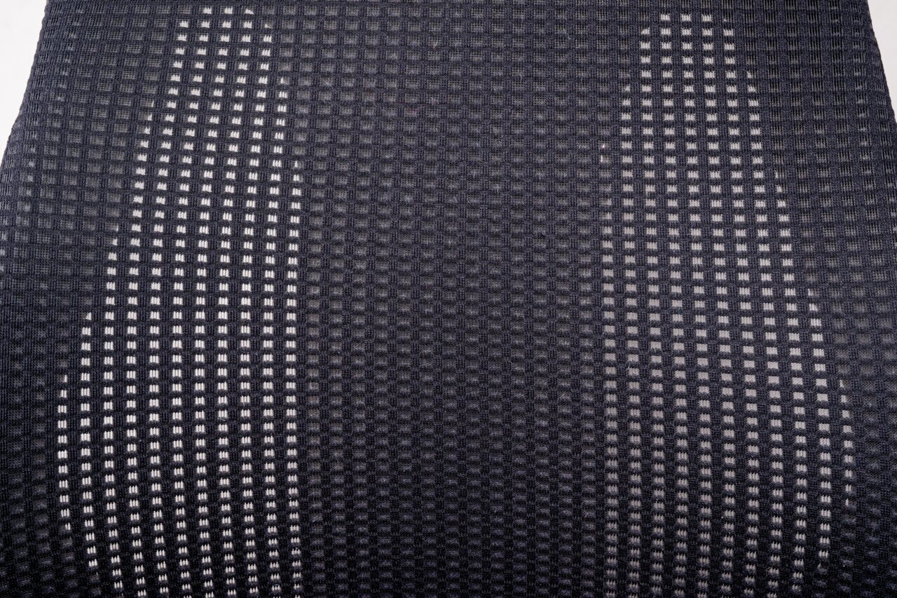 Nahaufnahme der Rückenlehne eines Drehstuhls mit grauem, gitterartigem Stoffmuster, von vorne betrachtet.