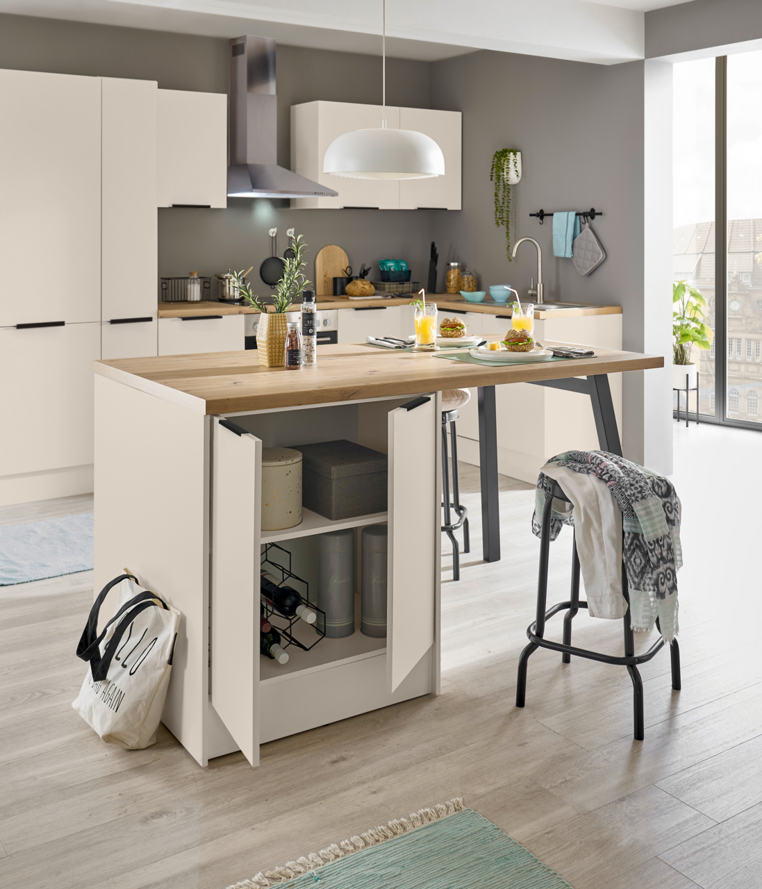 Moderne weiße Küche mit Kücheninsel und Holzarbeitsplatte, offene Unterschranktüren mit Stauraum und Weinregal, Barhocker und gedeckter Frühstückstisch; Perspektive: frontale leicht seitliche Ansicht auf Augenhöhe.