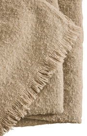 Nahaufnahme einer beigen Wohndecke mit Fransen, gefaltet und aus einer seitlichen Perspektive fotografiert.