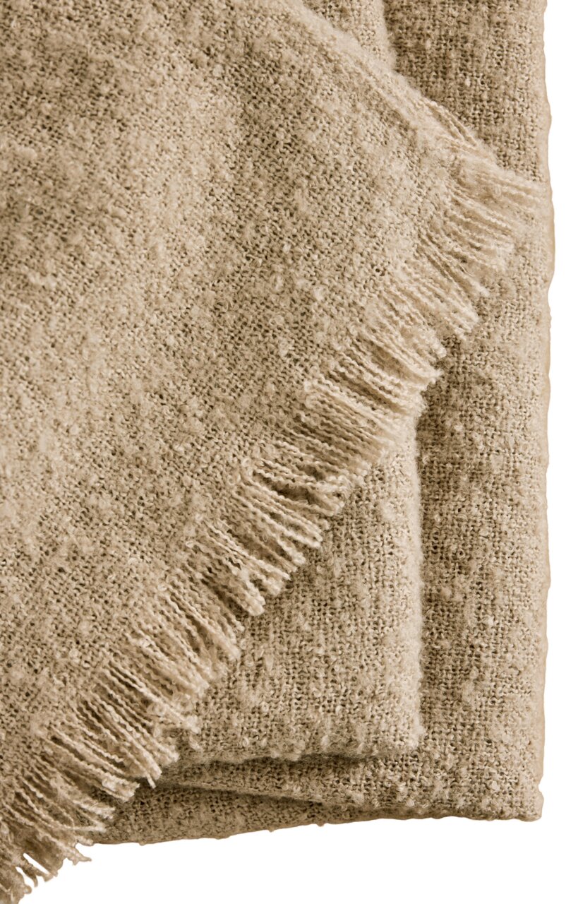 Nahaufnahme einer beigen Wohndecke mit Fransen, gefaltet und aus einer seitlichen Perspektive fotografiert.