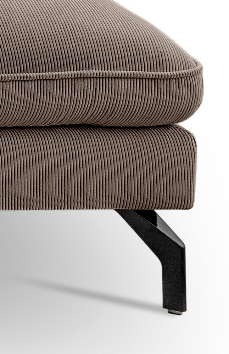 Detailaufnahme aus seitlicher Perspektive: gepolsterter Hocker oder Ottoman mit taupefarbenem Cordbezug, sichtbarer Naht und schwarzem Metallfuß