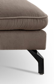 Detailaufnahme aus seitlicher Perspektive: gepolsterter Hocker oder Ottoman mit taupefarbenem Cordbezug, sichtbarer Naht und schwarzem Metallfuß