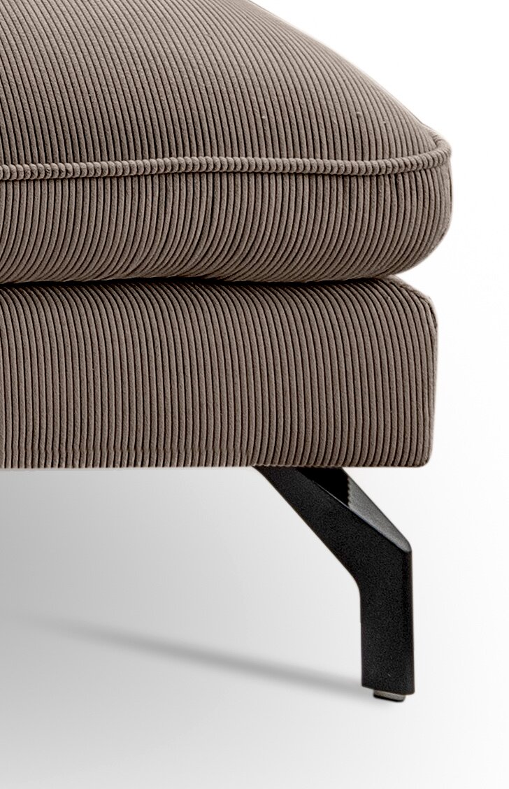 Detailaufnahme aus seitlicher Perspektive: gepolsterter Hocker oder Ottoman mit taupefarbenem Cordbezug, sichtbarer Naht und schwarzem Metallfuß