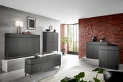 Moderne, dunkelgraue Kommode in einem stilvollen Wohnzimmer mit Ziegelwand und großen Fenstern, seitliche Perspektive.