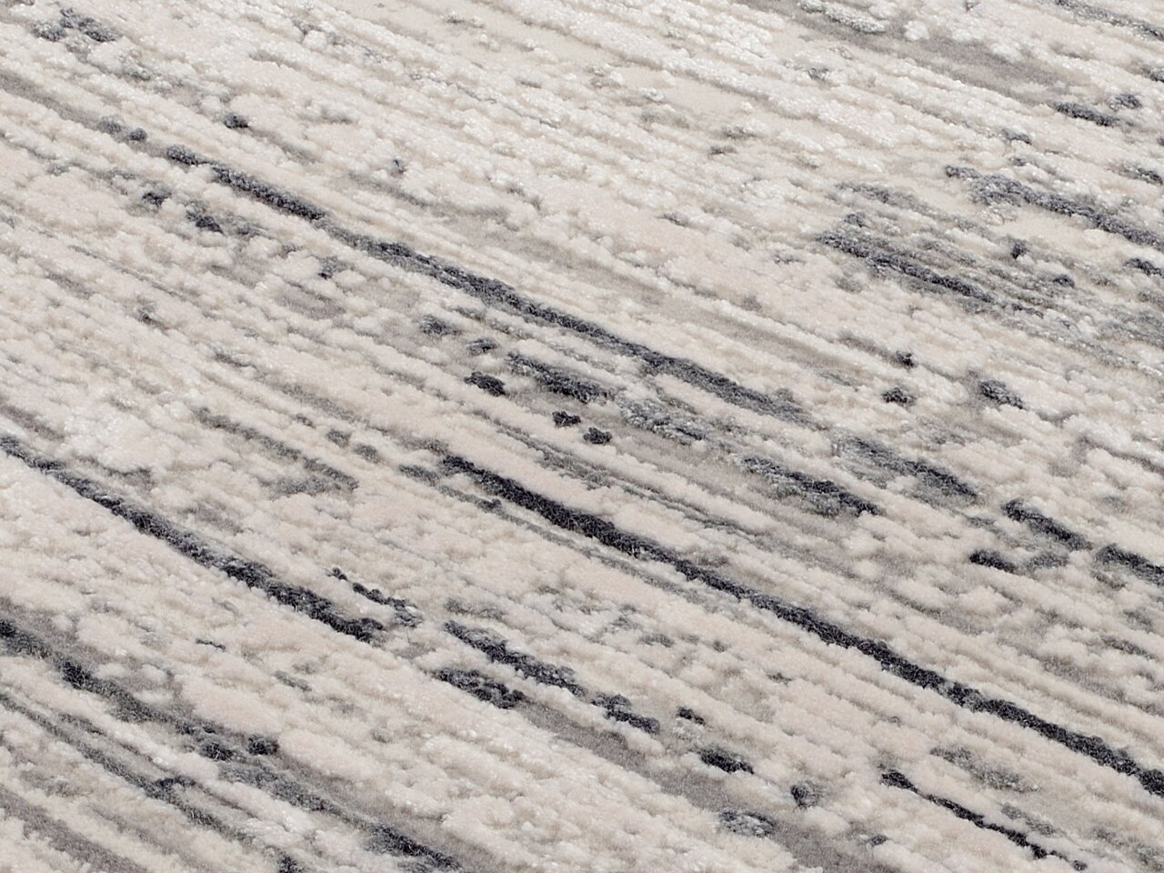 Nahaufnahme eines Designer Teppichs mit abstraktem Muster in Grautönen, von oben betrachtet.