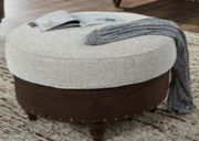 Runder Hocker mit heller Polsterung und dunklem Holzsockel, von schräg oben fotografiert, mit einem Buch und einer Decke darauf.