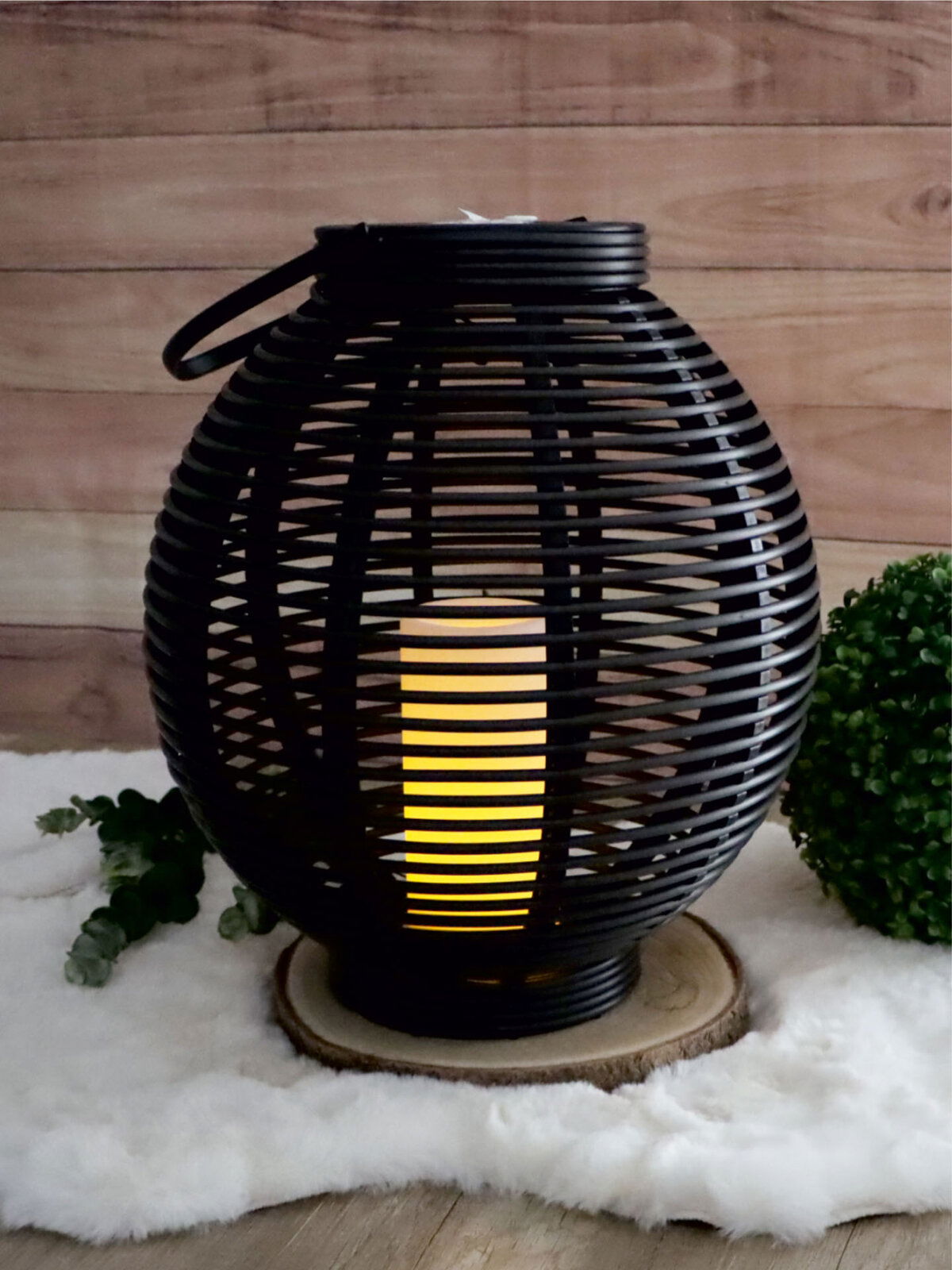 Runde Solar Laterne in Rattan-Optik mit warmem Licht, auf einem Holzuntersetzer stehend, seitliche Perspektive