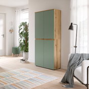 Hoher zweitüriger Schrank mit salbeigrünen Fronten und Korpus in heller Holzoptik, im Wohnzimmer platziert; Perspektive: frontale Ansicht mit leichtem Blick von rechts.