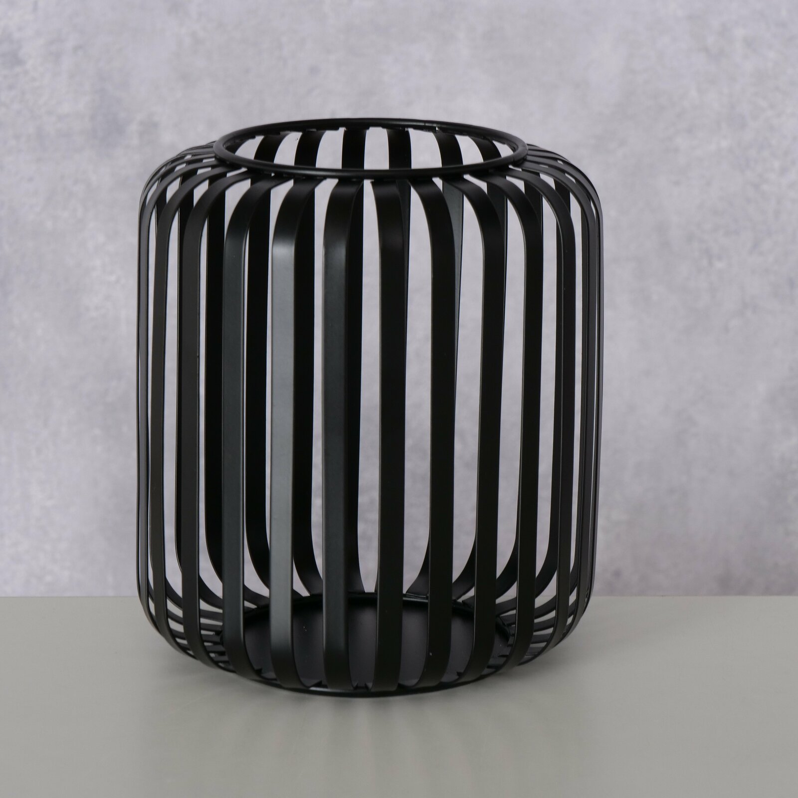 Schwarzes, rundes Windlicht aus Metall mit vertikalen Streben, seitliche Perspektive.