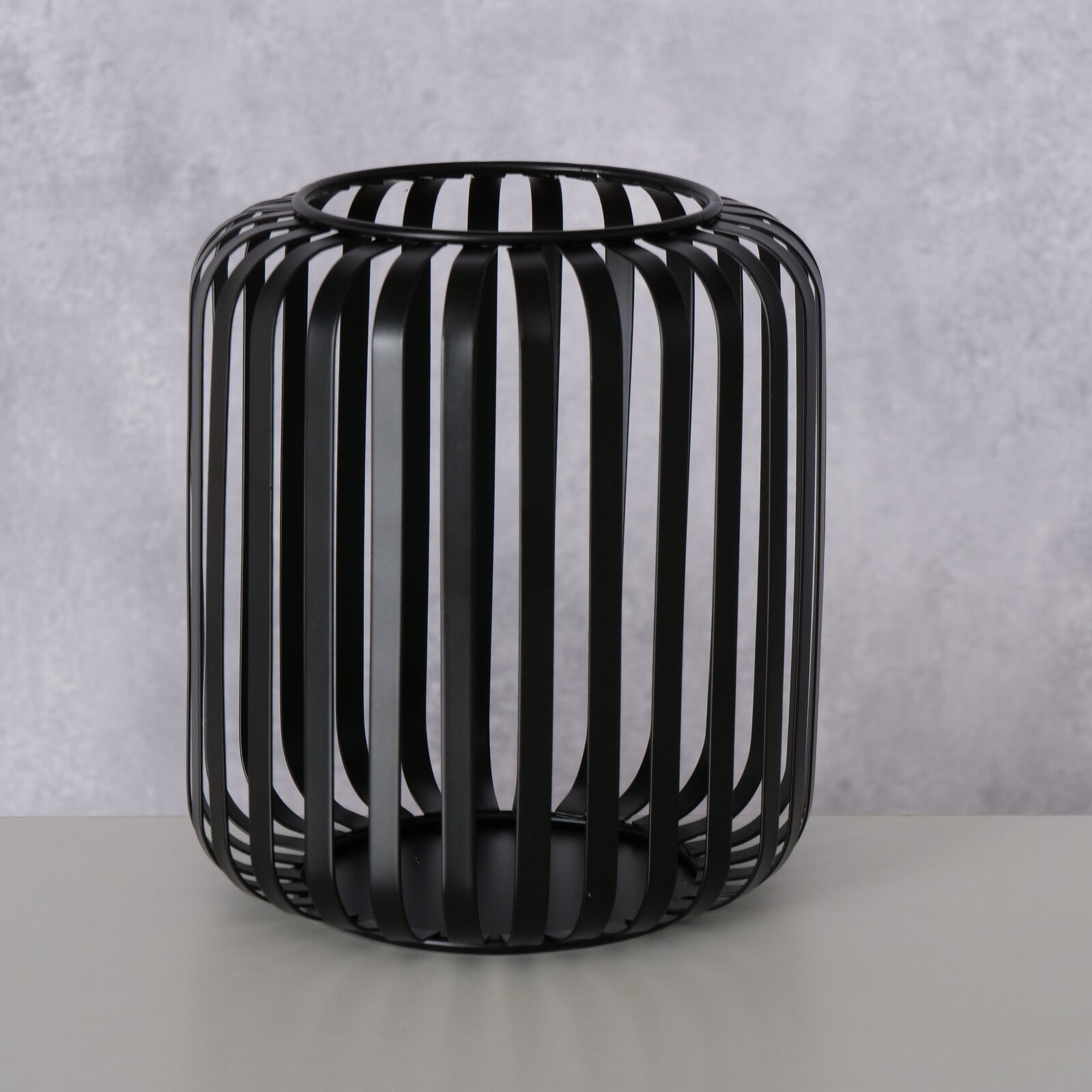 Schwarzes, rundes Windlicht aus Metall mit vertikalen Streben, seitliche Perspektive.