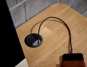 Nahaufnahme eines E-Schreibtischs mit Kabeldurchführung und Ladekabel, von oben betrachtet.