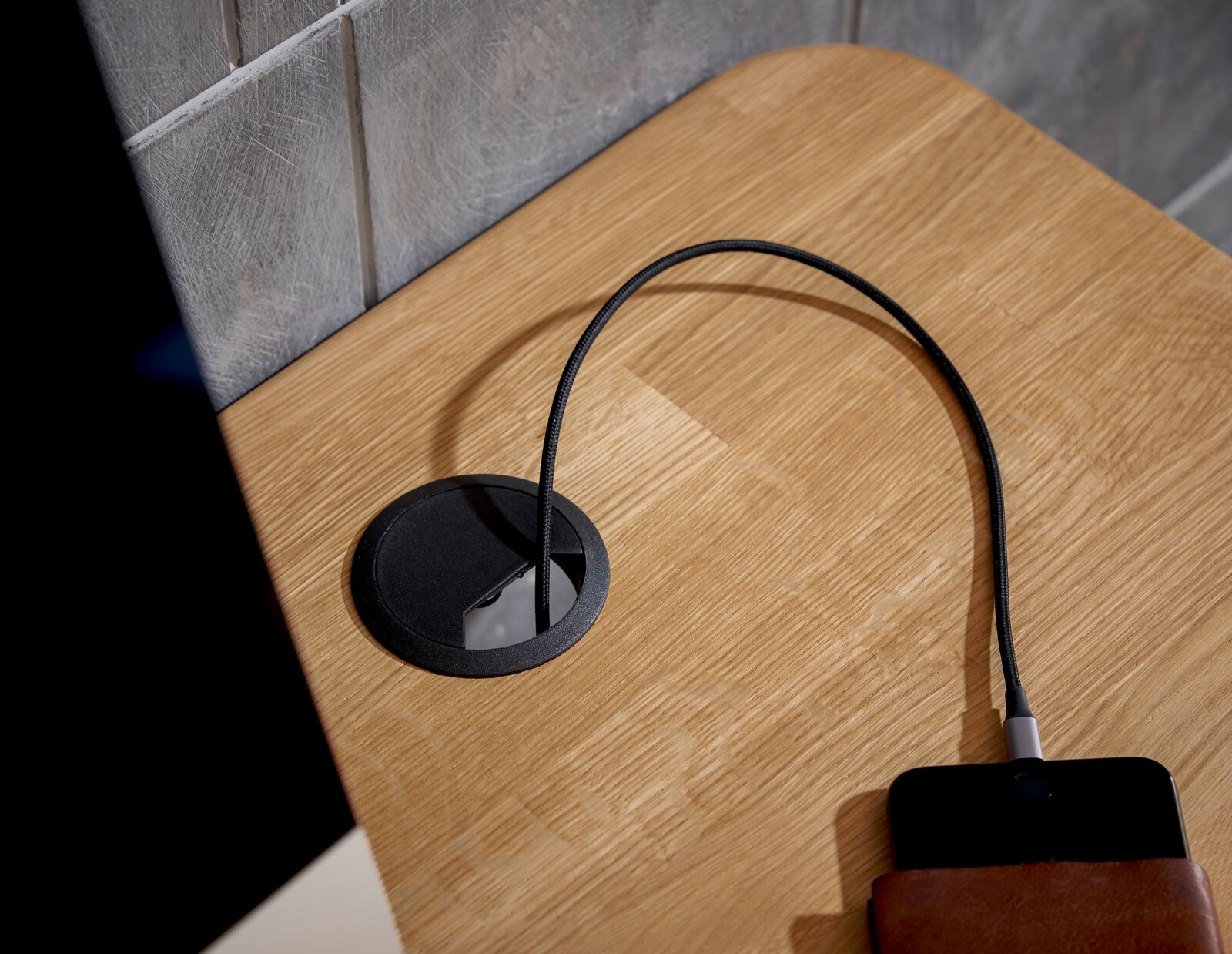 Nahaufnahme eines E-Schreibtischs mit Kabeldurchführung und Ladekabel, von oben betrachtet.