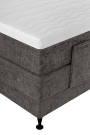 Detailaanzicht vanuit schuin bovenperspectief van een donkergrijs gestoffeerd boxspringbed met wit, golvend doorgestikt matras en zwarte poot