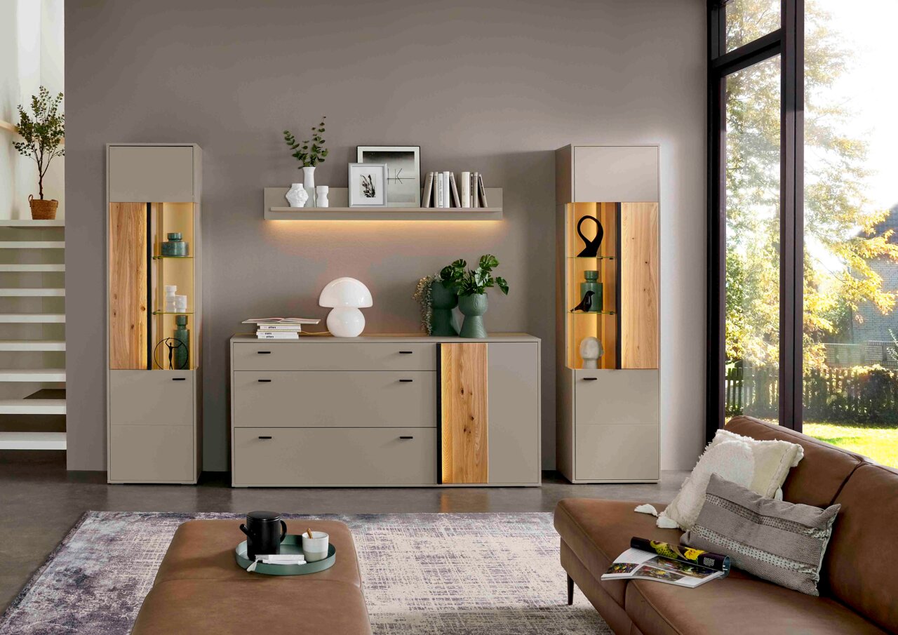 Moderne vitrinekast voor in de woonkamer van licht hout en glas, gefotografeerd vanaf de voorkant, met decoratieve elementen en verlichting.