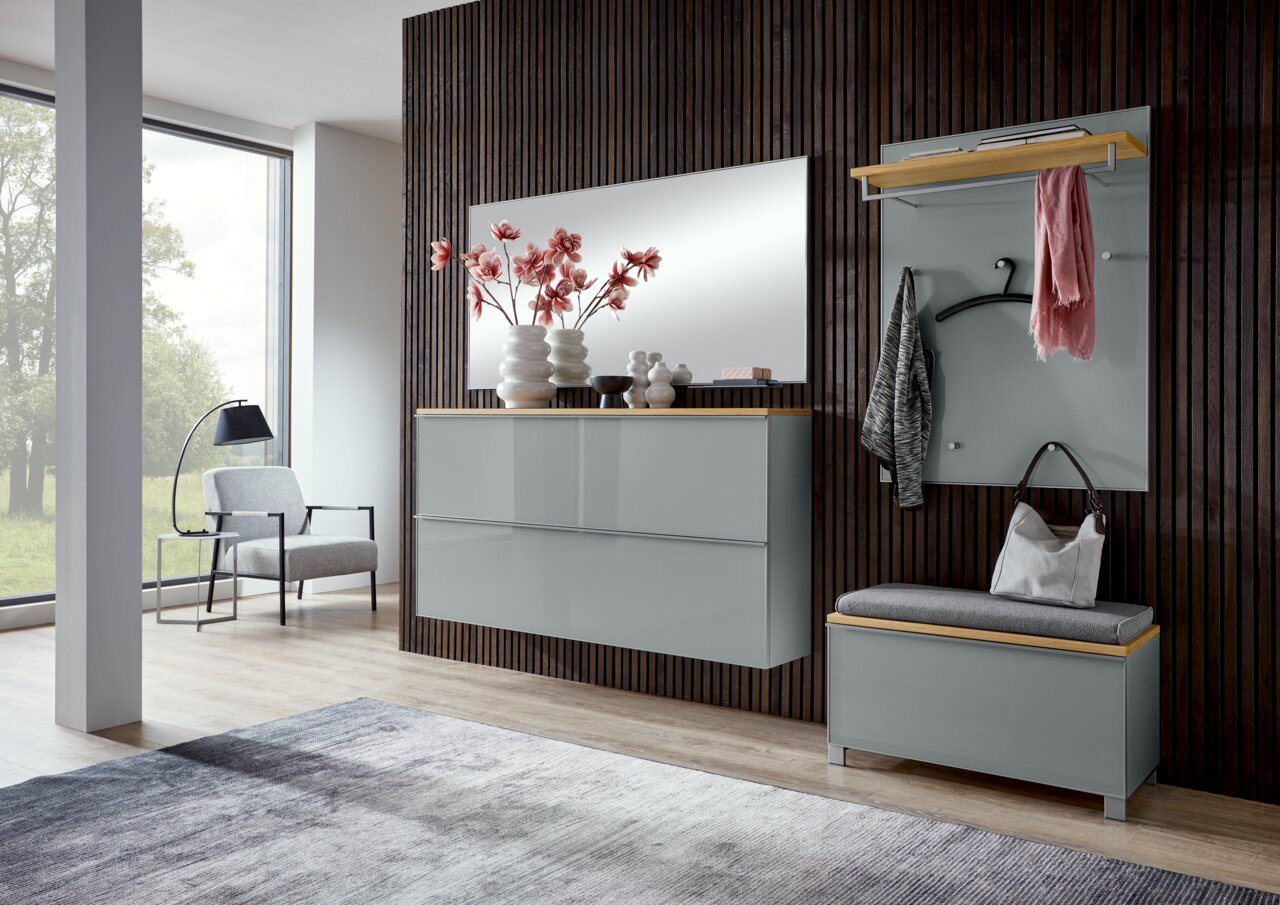 Moderne Garderoben-Kombination im Flur: graue, wandhängende Kommode mit großem Spiegel und Deko sowie Garderobenpaneel mit Hutablage, Kleiderbügeln und Sitzbank mit Polster vor dunkler Holzlamellenwand, gezeigt in frontaler Perspektive.