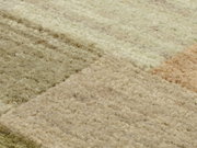 Nahaufnahme eines Wollteppichs mit verschiedenen Beige- und Brauntönen in einem geometrischen Muster, von oben betrachtet.