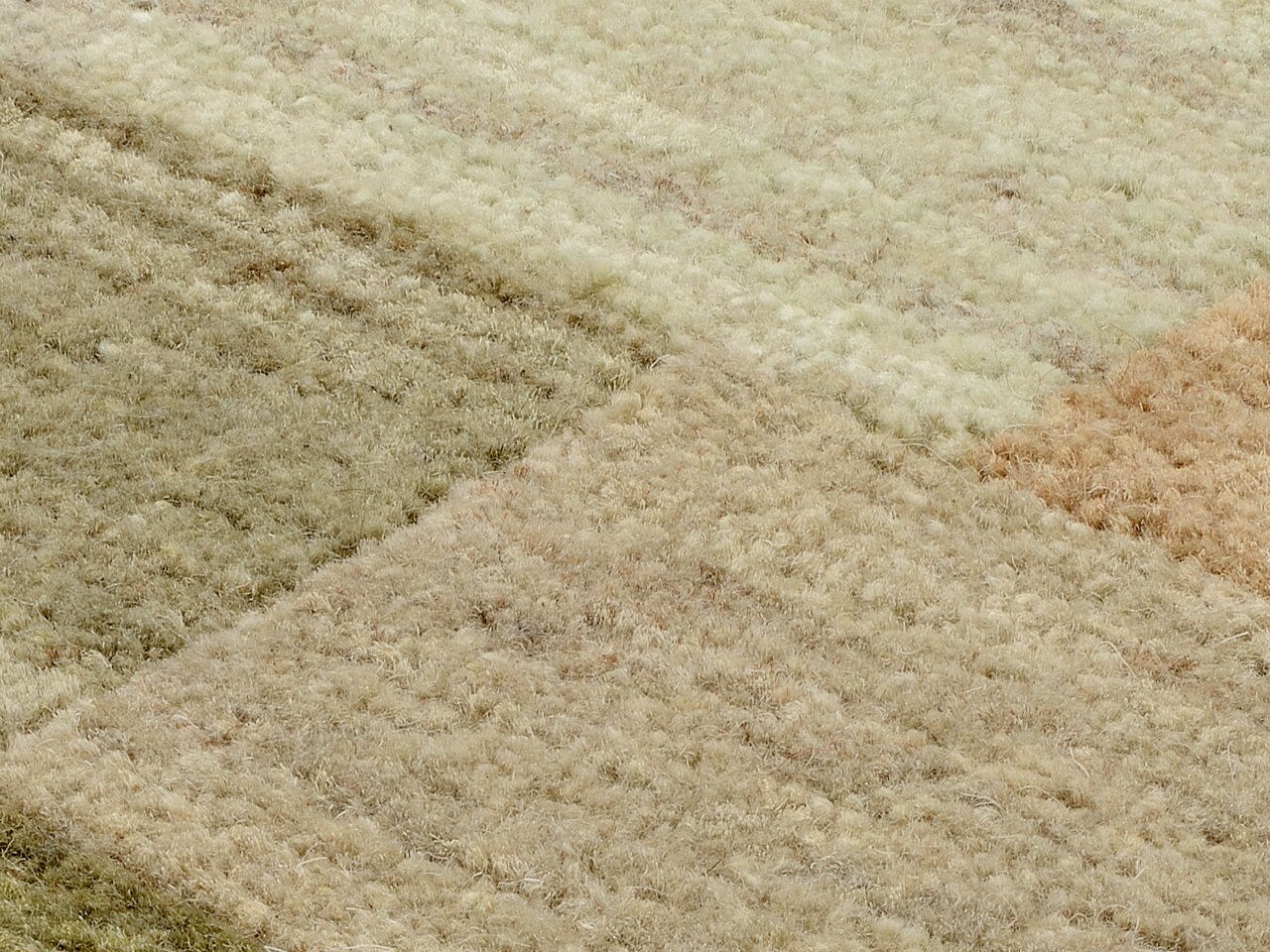 Nahaufnahme eines Wollteppichs mit verschiedenen Beige- und Brauntönen in einem geometrischen Muster, von oben betrachtet.